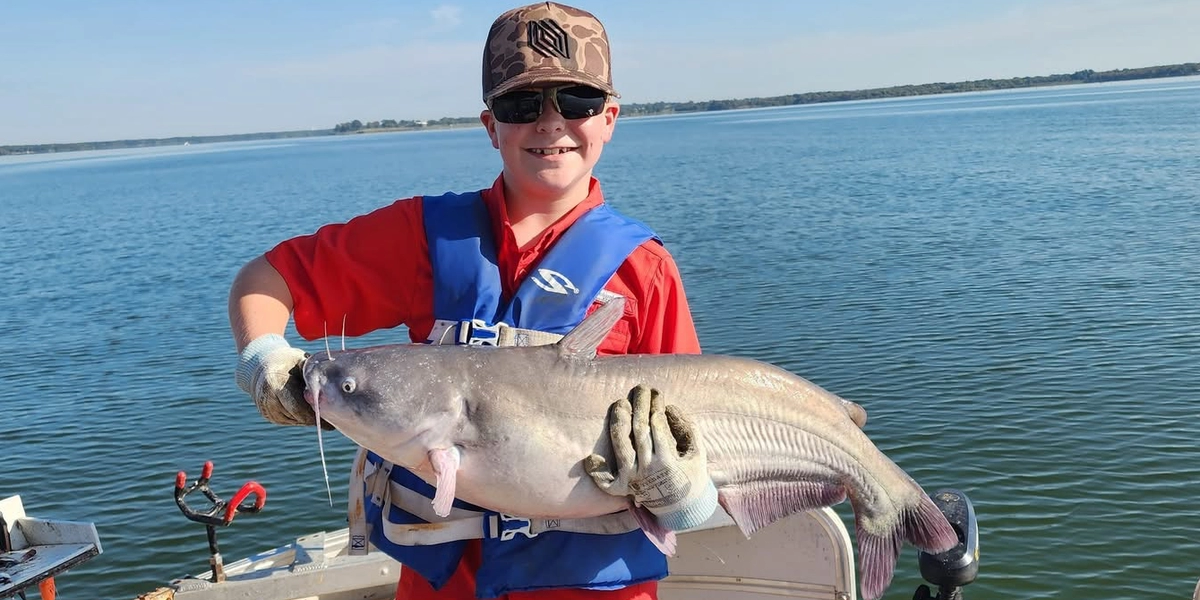 Young angler holding a large blue catfish on a boat at Lake Tawakoni under clear skies.